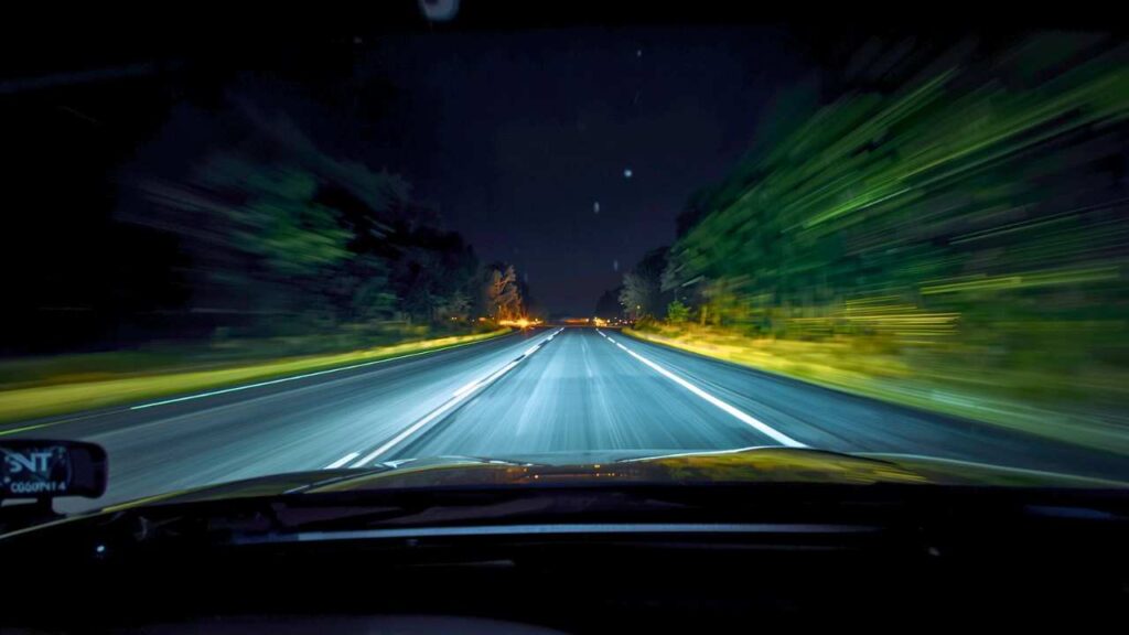 Night highway view from driver’s seat with bright headlights, illustrating difficulty seeing while driving at night and the need for an eye checkup.